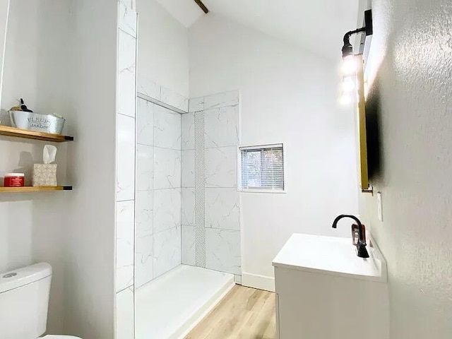 bathroom with a tile shower, wood-type flooring, lofted ceiling, vanity, and toilet