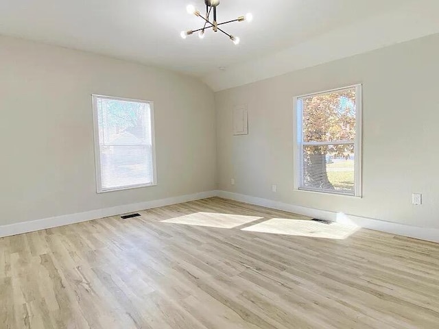 empty room featuring an inviting chandelier, plenty of natural light, and light hardwood / wood-style flooring