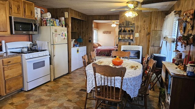 kitchen featuring ceiling fan, wooden walls, heating unit, and white appliances