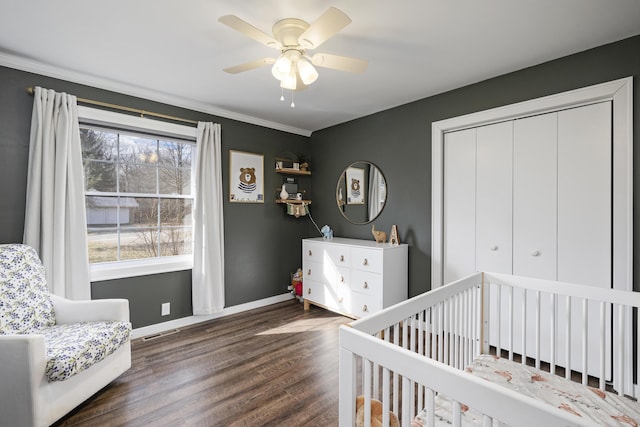 bedroom featuring crown molding, a crib, ceiling fan, dark hardwood / wood-style floors, and a closet