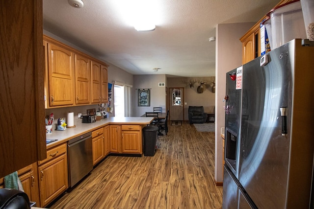 kitchen featuring stainless steel appliances, kitchen peninsula, hardwood / wood-style floors, and a textured ceiling