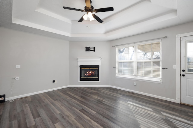 unfurnished living room featuring dark wood-type flooring, ceiling fan, and a raised ceiling