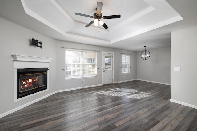 unfurnished living room featuring a tray ceiling, dark wood-type flooring, and ceiling fan with notable chandelier