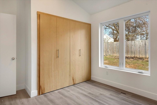 unfurnished bedroom featuring a closet, lofted ceiling, multiple windows, and light hardwood / wood-style flooring