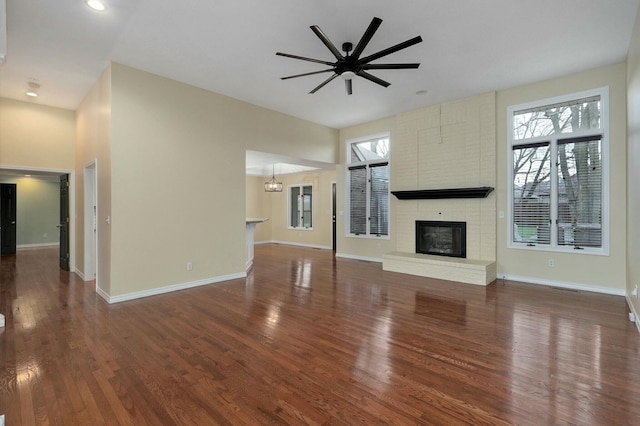 unfurnished living room with dark hardwood / wood-style flooring, a brick fireplace, and a wealth of natural light