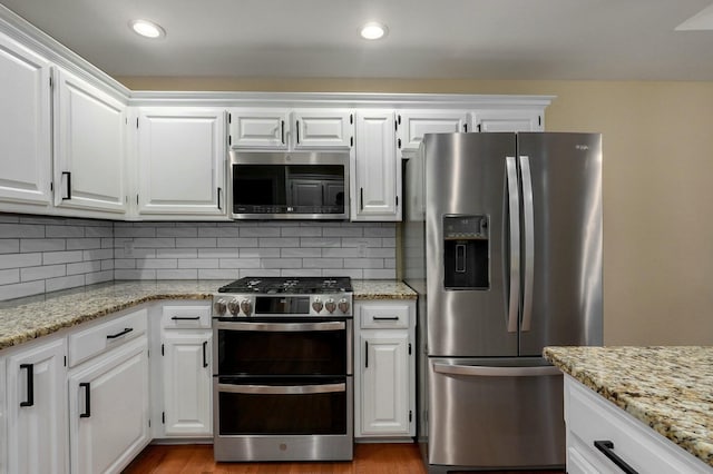 kitchen featuring appliances with stainless steel finishes, white cabinets, backsplash, light stone counters, and light hardwood / wood-style floors