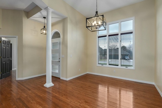 unfurnished dining area with decorative columns, wood-type flooring, and a chandelier