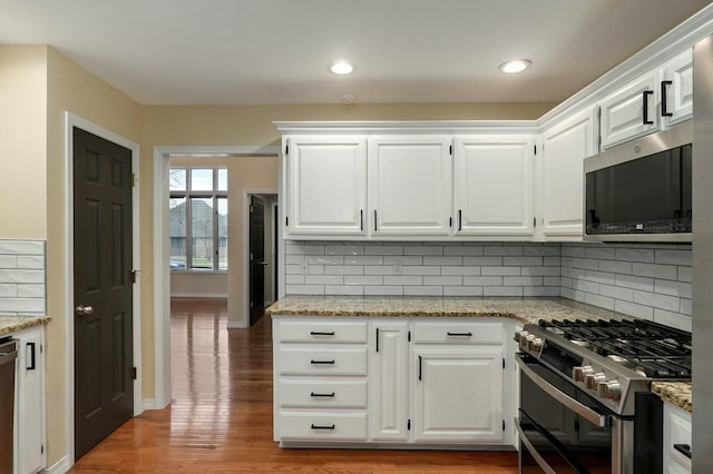 kitchen with appliances with stainless steel finishes, hardwood / wood-style floors, white cabinetry, decorative backsplash, and light stone counters