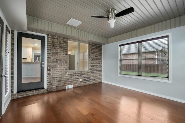 empty room with hardwood / wood-style flooring, ceiling fan, brick wall, and wooden ceiling