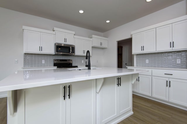 kitchen featuring sink, wood-type flooring, appliances with stainless steel finishes, white cabinets, and backsplash