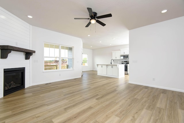 unfurnished living room featuring ceiling fan, a large fireplace, and light hardwood / wood-style flooring