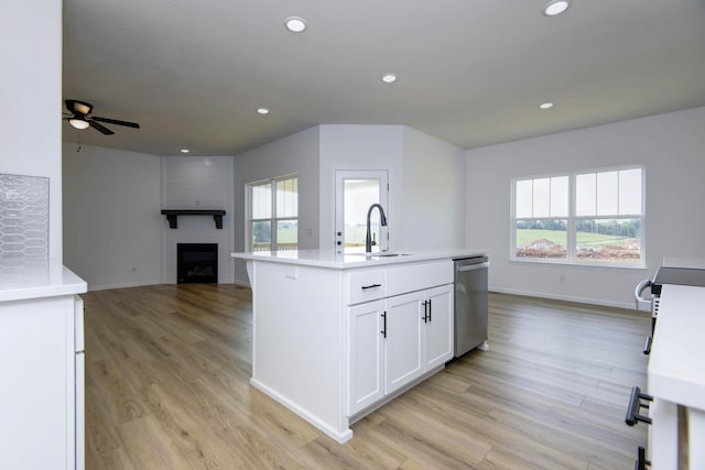 kitchen featuring appliances with stainless steel finishes, a fireplace, white cabinetry, an island with sink, and sink