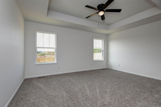 unfurnished room with a raised ceiling, ceiling fan, and carpet