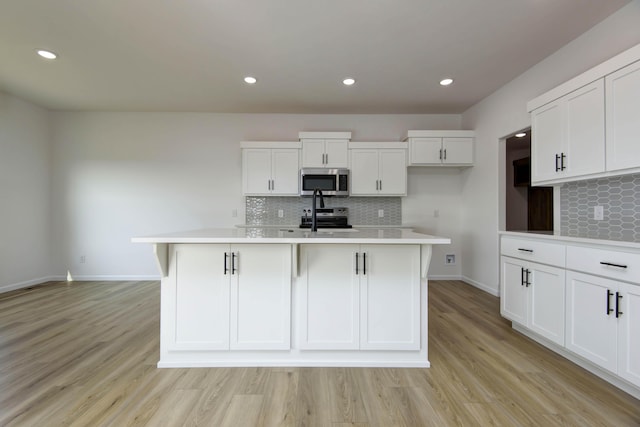 kitchen featuring an island with sink, appliances with stainless steel finishes, white cabinets, and light hardwood / wood-style floors