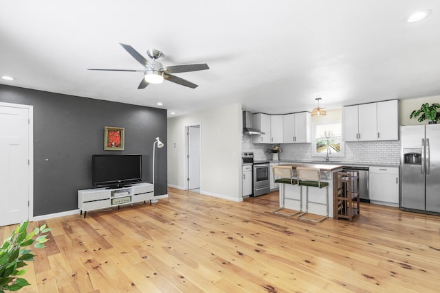 kitchen featuring wall chimney exhaust hood, a breakfast bar area, decorative light fixtures, a center island, and stainless steel appliances