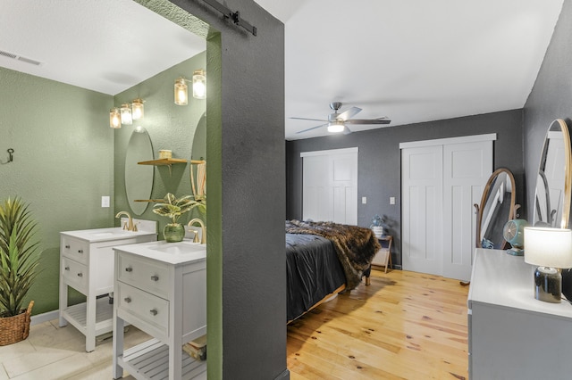 bedroom with multiple closets, ceiling fan, light hardwood / wood-style floors, and sink