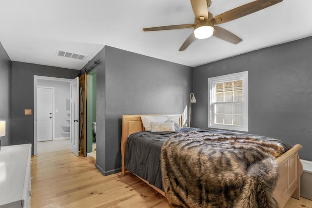 bedroom featuring ceiling fan, a barn door, and light wood-type flooring