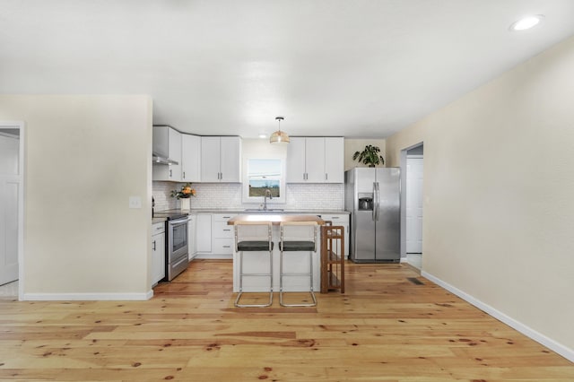 kitchen featuring a breakfast bar, white cabinetry, a center island, hanging light fixtures, and appliances with stainless steel finishes