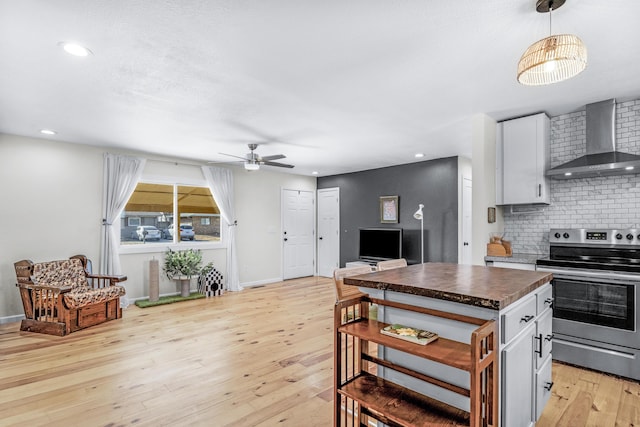 kitchen with wall chimney exhaust hood, white cabinetry, tasteful backsplash, light hardwood / wood-style flooring, and electric stove