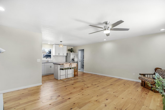 unfurnished living room featuring sink, ceiling fan, and light wood-type flooring