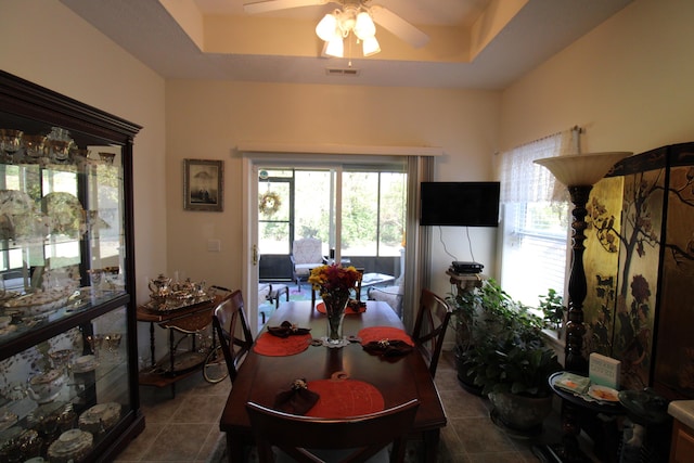 tiled dining space with ceiling fan and a raised ceiling