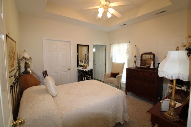 carpeted bedroom with a raised ceiling and ceiling fan