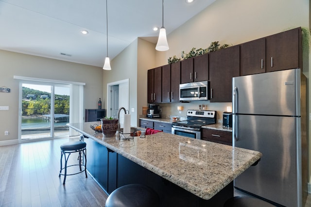 kitchen featuring appliances with stainless steel finishes, a kitchen breakfast bar, a high ceiling, dark brown cabinetry, and a center island with sink