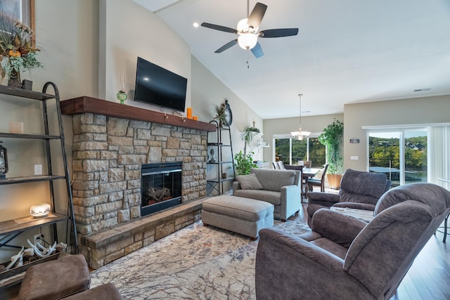 living room with lofted ceiling, hardwood / wood-style floors, a stone fireplace, and ceiling fan with notable chandelier