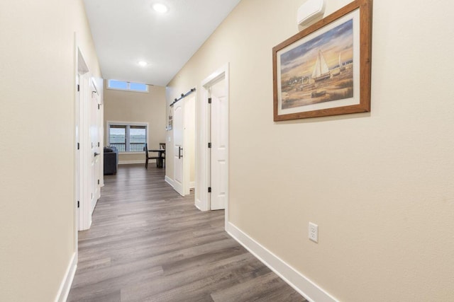 hall with a barn door, recessed lighting, wood finished floors, and baseboards