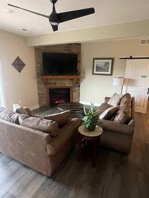 living area featuring visible vents, a large fireplace, ceiling fan, a barn door, and wood finished floors