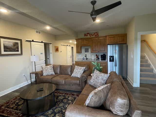 living room featuring visible vents, a barn door, stairway, baseboards, and ceiling fan