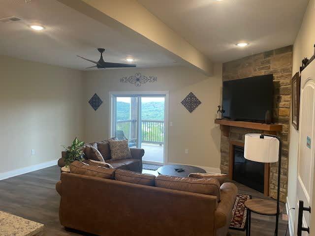 living room with baseboards, beam ceiling, a fireplace, ceiling fan, and dark wood-type flooring