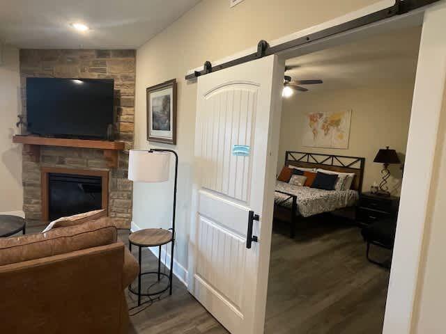 bedroom with a barn door, a stone fireplace, and wood finished floors