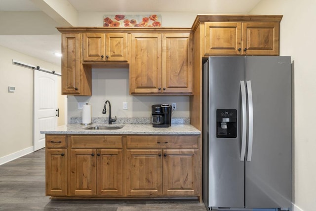 kitchen featuring light stone counters, dark wood-style flooring, a sink, a barn door, and stainless steel fridge