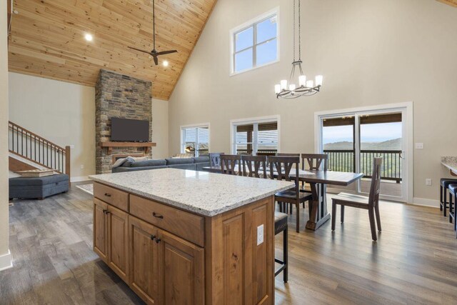 kitchen with brown cabinetry, dark wood-style floors, a stone fireplace, wood ceiling, and a kitchen breakfast bar