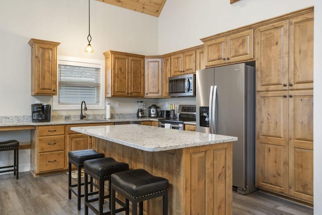 kitchen with pendant lighting, appliances with stainless steel finishes, light stone countertops, and a kitchen island