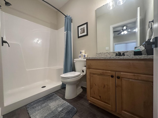 bathroom with toilet, a stall shower, wood finished floors, vanity, and a ceiling fan