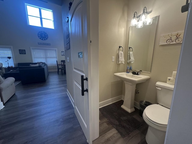 half bath featuring baseboards, toilet, a high ceiling, and wood finished floors