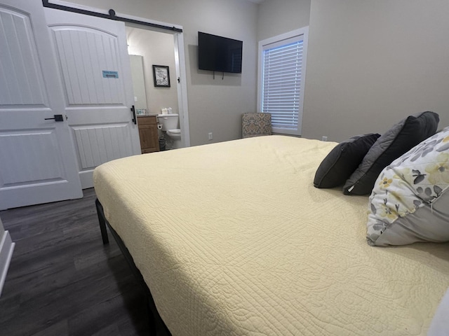 bedroom featuring a barn door, dark wood-style floors, and ensuite bathroom