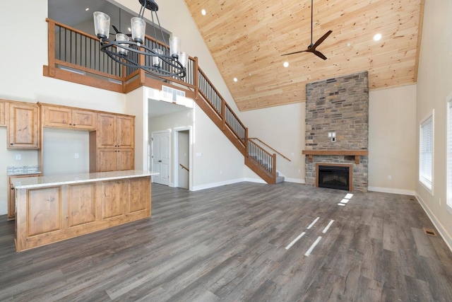 unfurnished living room featuring stairway, a stone fireplace, baseboards, wood ceiling, and dark wood-style flooring