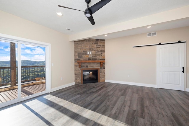 unfurnished living room featuring visible vents, wood finished floors, a barn door, a stone fireplace, and baseboards