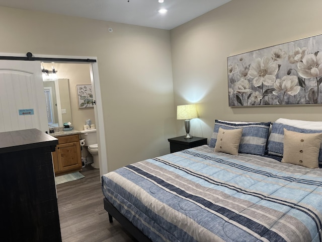 bedroom featuring recessed lighting, a barn door, dark wood-type flooring, and ensuite bath