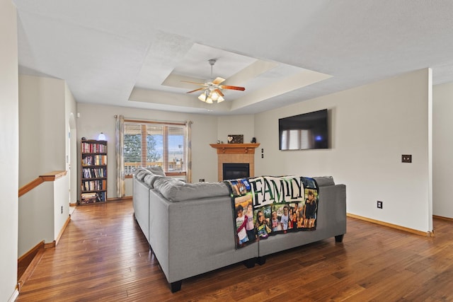 living room featuring a raised ceiling, a tile fireplace, ceiling fan, and dark hardwood / wood-style flooring