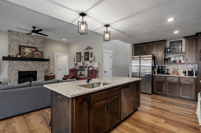 kitchen featuring sink, appliances with stainless steel finishes, a kitchen island with sink, dark brown cabinets, and light wood-type flooring