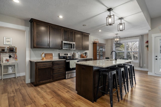 kitchen featuring a breakfast bar area, hanging light fixtures, a kitchen island with sink, stainless steel appliances, and light stone countertops