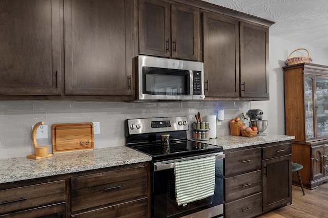 kitchen with light stone counters, tasteful backsplash, dark brown cabinets, stainless steel appliances, and light hardwood / wood-style floors