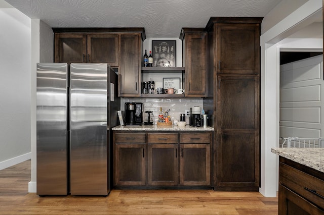 kitchen with light stone countertops, stainless steel fridge, and dark brown cabinetry