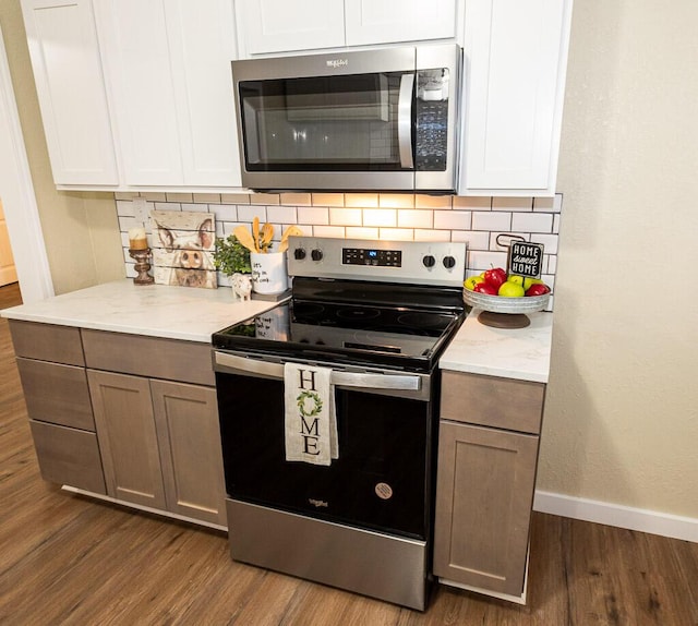 kitchen featuring dark wood-type flooring, white cabinetry, tasteful backsplash, stainless steel appliances, and light stone countertops