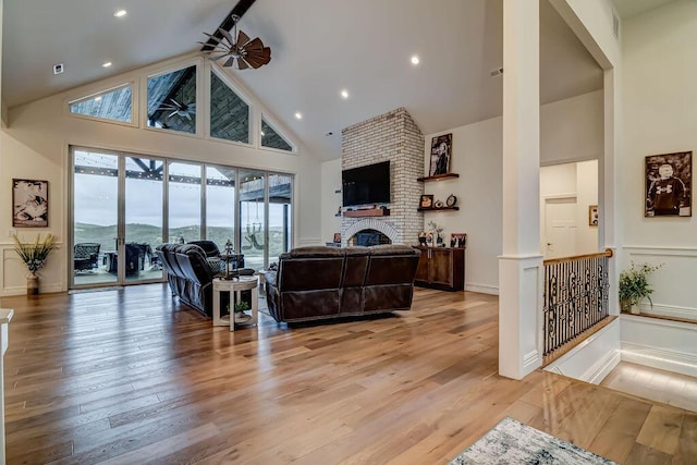 living room featuring ceiling fan, a fireplace, light hardwood / wood-style floors, and high vaulted ceiling