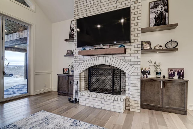 living room featuring lofted ceiling, a brick fireplace, and light wood-type flooring